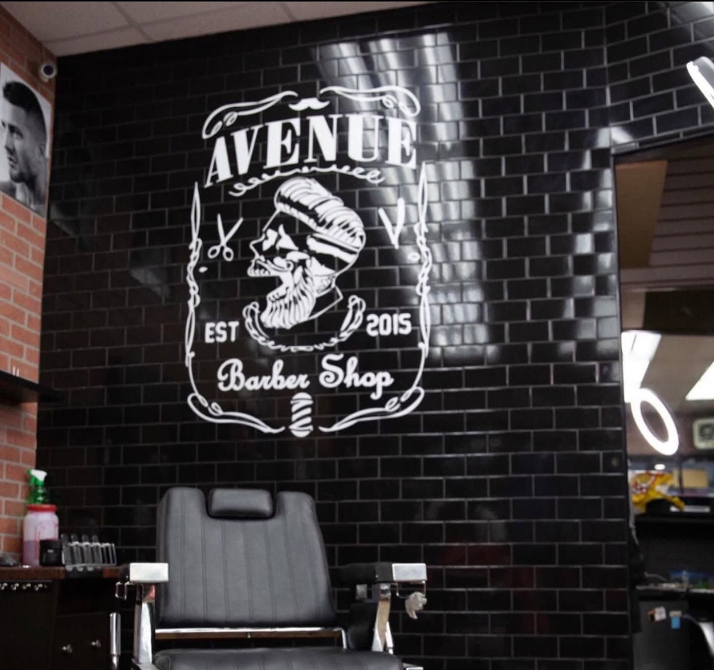 A black leather barber chair in front of the Avenue Barber Shop logo on black subway tile
