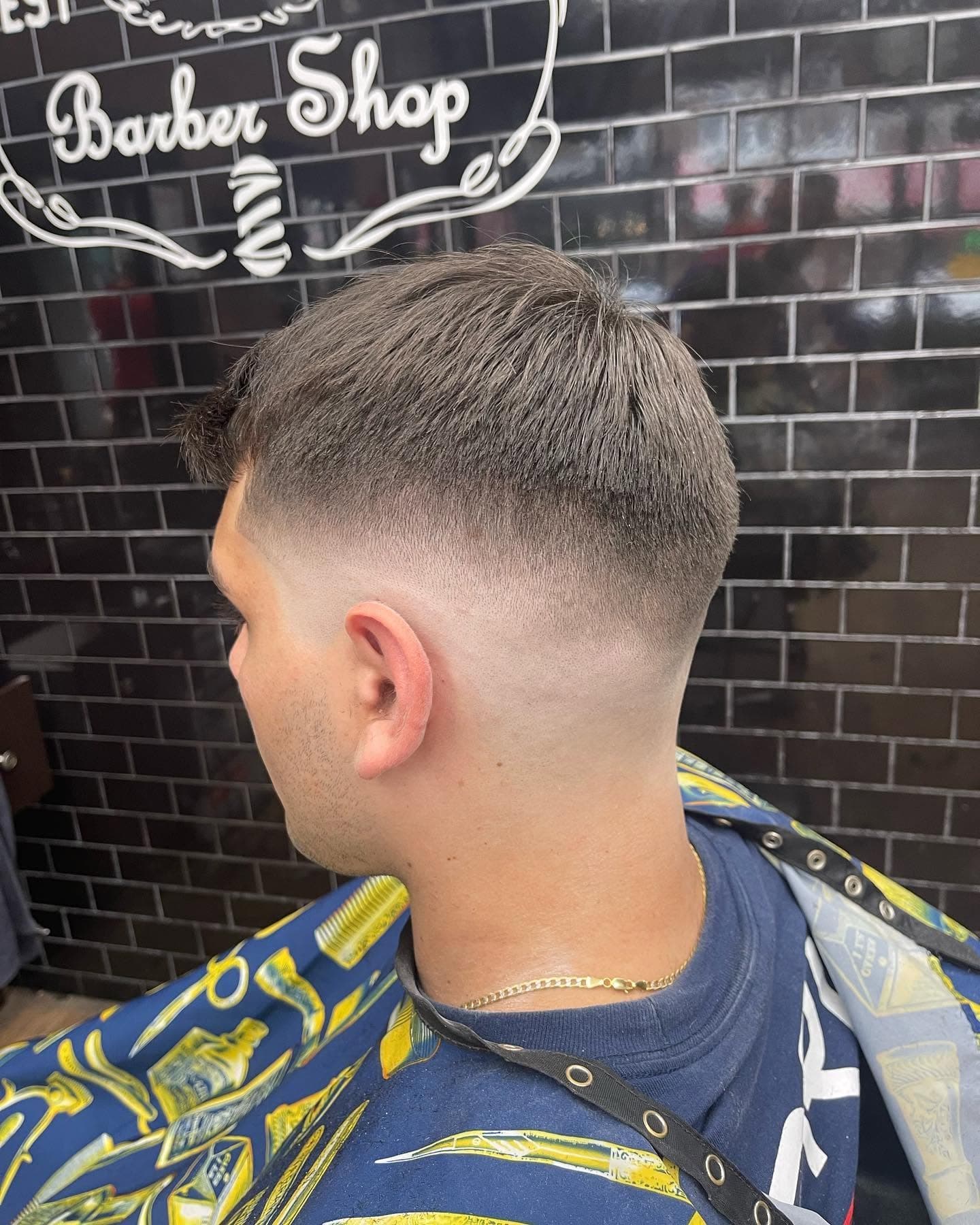A mid fade seen from the side, in front of the shop's subway tile wall